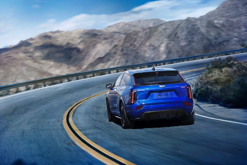 Rear View of a Blue 2026 OPTIQ-V Driving on a Curve of a Mountain Row | Flow Cadillac of Wilmington in Wilmington NC