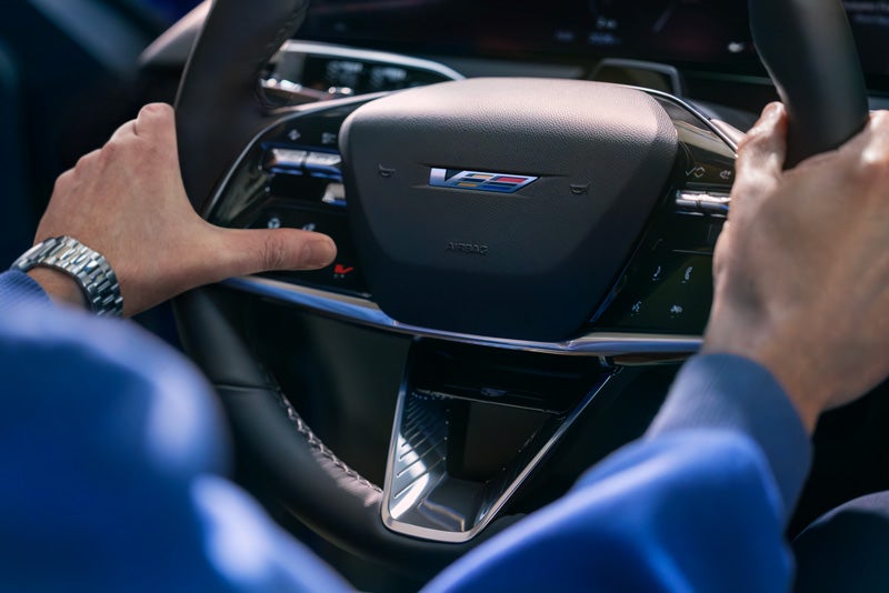 Close-up of a Man About to Press the V-Button on the 2026 OPTIQ-V Steering Wheel | Flow Cadillac of Wilmington in Wilmington NC